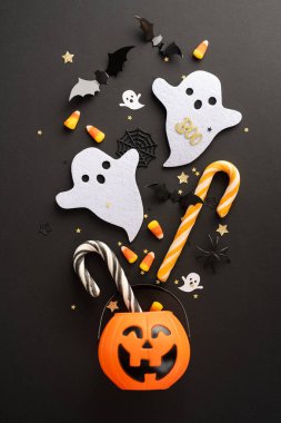 Tatlı hayalet figürleri, şeker mısır, nane şekeri çubukları, yarasalar ve siyah bir yüzey üzerinde gülümseyen bir balkabağı kovası olan bayram dikey arka planı.