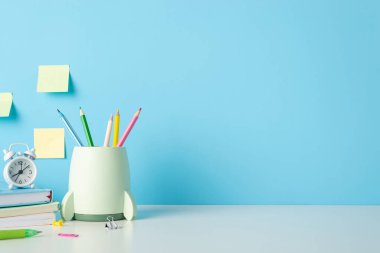 Renkli kağıda, yapışkan notlara, kitaplara ve saate sahip okul konseptine mavi arkaplanlı beyaz bir masanın üzerindeki
