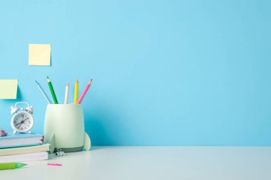 Renkli kağıtları, saati ve mavi arka planda yapışkan notları olan düzenli bir masa. Okul temaları için ideal