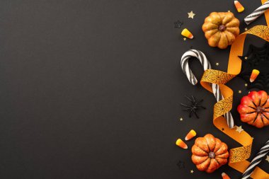 Cadılar Bayramı temalı resimde balkabağı, mısır şekeri, siyah ve beyaz baston şekerler, turuncu kurdele ve siyah arka planda dekoratif yıldızlar yer alıyor.