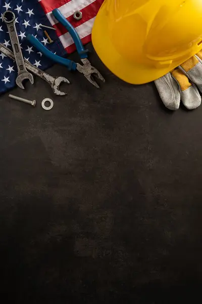 stock image Yellow hard hat, tools, and American flag on a dark vertical background symbolizing Labor Day in USA