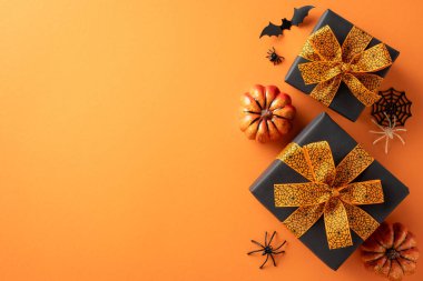 Cadılar Bayramı hediyeleri turuncu kurdeleli siyah kağıda sarılmış, turuncu arka planda örümcek ve balkabağı süslemeleri eşliğinde.