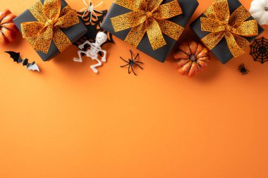 Cadılar Bayramı temalı hediye kutularının üst görüntüsü içinde balkabakları, iskeletler, yarasalar ve parlak turuncu arka planda örümcekler var.