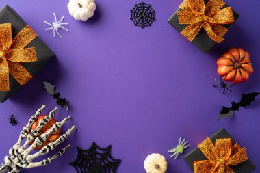 Cadılar Bayramı temalı resimde hediye kutuları, dekoratif balkabakları ve mor arka planda ürkütücü elementler yer alıyor.