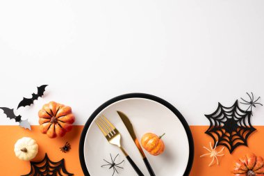 Beyaz ve turuncu arka planda balkabakları, örümcek ağları ve çatal bıçak takımlarının yer aldığı bayram masası.