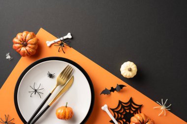 Siyah ve turuncu bir masa üzerinde balkabakları, örümcekler ve çatal bıçakların yer aldığı bayram yemeği düzeni.