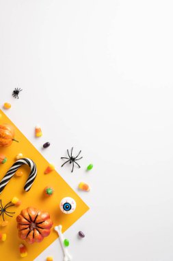 Turuncu bir yüzeye yerleştirilmiş çeşitli dikey Cadılar Bayramı şekerlemeleri ve ürkütücü dekorasyonlar, bayram teması için mükemmel.