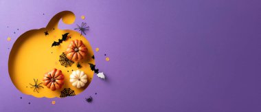 Canlı turuncu ve mor arka planda küçük balkabakları, yarasalar ve örümceklerden oluşan şık bir Cadılar Bayramı kartı tasarımı