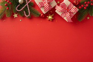 Şenlikli bir Noel sahnesinin en üst görüntüsü. Paketli hediyeler, baston şekerler ve kırmızı arka planda süsler.