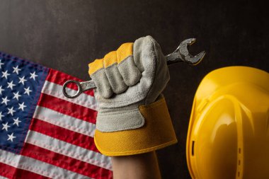 Amerika 'da İşçi Bayramı' nı sembolize eden, Amerikan bayrağının yanında İngiliz anahtarı ve sarı bir şapka tutan bir iş eldiveni.