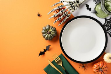 İskelet elli, balkabaklı ve turuncu arka planda şenlikli dekorasyonlu Cadılar Bayramı temalı masa ortamının en üst görüntüsü.