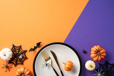 Cadılar Bayramı temalı masa ortamının en üst görüntüsü balkabakları, çatal bıçak takımı ve renkli arka planda ürkütücü dekorasyonlar.