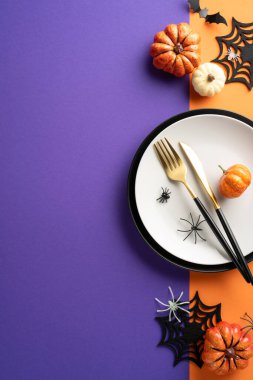 Cadılar Bayramı dikey masa ayarı, balkabakları, örümcek süslemeleri ve mor ve turuncu arka planda çatal bıçak takımı.