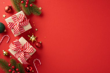 Kırmızı kurdeleli güzel Noel hediyelerinin üst görüntüsü yıldızlar, baston şekerler ve kırmızı arkaplandaki çam dalları gibi şenlikli süslemelerle çevrili.