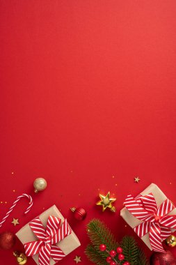Canlı dikey Noel düzenleme paketlenmiş hediyeler, dekoratif süsler ve kırmızı arka planda çam dalları, bayram ruhunu vurgulayarak