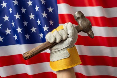 Amerikan bayrağının önünde çekiç tutan eldivenli el, İşçi Bayramı 'nı ve işçilerin gücünü simgeliyor.