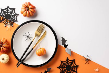 Balkabakları, siyah çatal bıçak takımı, örümcek ağı süslemeleri ve turuncu ve beyaz bir yüzey üzerinde ürkütücü elementler içeren zarif bir Cadılar Bayramı sofrası.