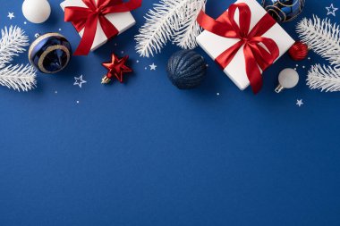 Süslü, kırmızı kurdeleli beyaz hediyeler ve mavi arka planda şenlikli yeşillikler içeren dekoratif bir Noel ortamı.