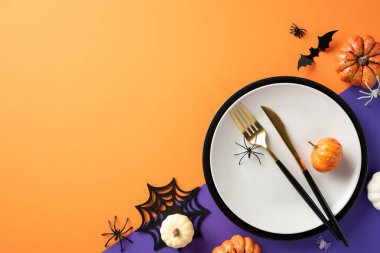 Beyaz tabak, balkabağı, yarasa ve turuncu arka planda örümcek süslemeleri olan Cadılar Bayramı masası.