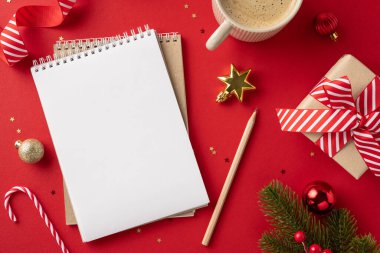 Kırmızı arka planda boş bir defter, kahve, hediye ve süsleme içeren Noel temalı bir masanın yukarıdan aşağı görüntüsü