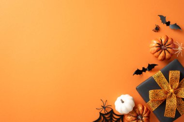 Cadılar Bayramı süslemeleri, balkabakları, yarasalar, örümcek ve turuncu arka planda kurdeleli bir hediye.