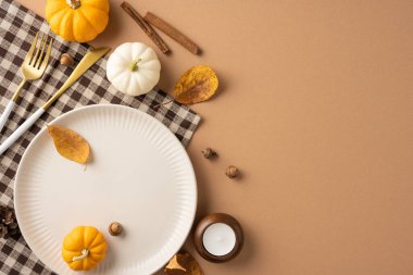 İçinde bir tabak, küçük balkabağı ve kahverengi arka planda sonbahar yaprakları olan bir Şükran Günü sofrası. Sahne, düşüşün sıcak ve davetkar atmosferini yakalar.