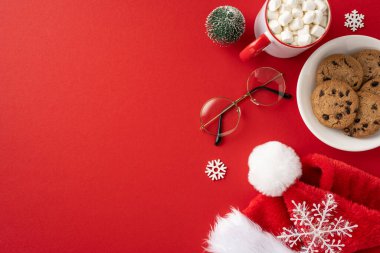 Noel Baba şapkası, bardaklar, kurabiyeler ve kırmızı arka planda şekerlemeler olan bir kupa sıcak kakao.