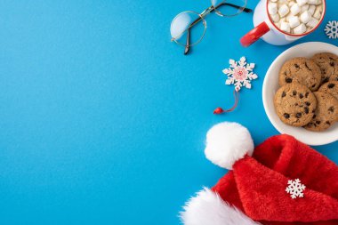 Kurabiyeli, şekerli ve kar taneli Noel Baba şapkası parlak mavi bir arka planda Noel ruhunu çağrıştırıyor.