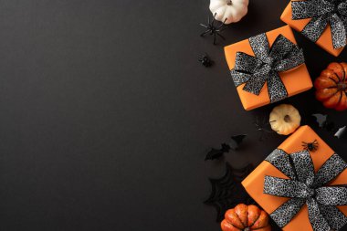 Cadılar Bayramı hediyeleri turuncu kağıda sarılmış siyah fiyonklarla çevrili küçük balkabakları ve siyah arka planda ürkütücü süslemelerle