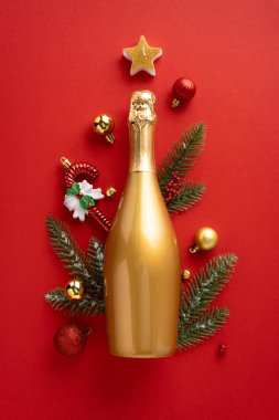 Altın dikey bir şampanya şişesi, parlak kırmızı arka planda, mücevherler ve çam dalları da dahil olmak üzere şenlikli Noel süslemeleriyle çevriliydi. Tatil sezonu ve yeni yılı kutlamak için mükemmel..