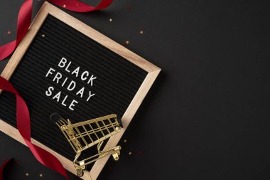 Minyatür alışveriş arabası ve kırmızı kurdeleli Kara Cuma tabelası. Bayram alışverişini ve indirimleri temsil ediyor.