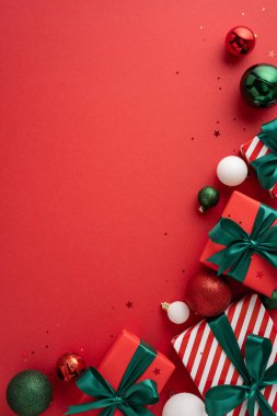 Kırmızı arka planda yeşil süslemelerle çevrili yeşil kurdelelerle süslenmiş şık Noel hediyeleri. Bayram kutlamaları ve şenlikli selamlar için mükemmel.