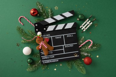 İçinde bir film alkış tahtası, baston şeker, zencefilli ekmek ve takılar bulunan Noel süslemeleri olan yaratıcı bir kompozisyon. Tatil temalı sinematik projeler ve mevsimsel kutlamalar için mükemmel.