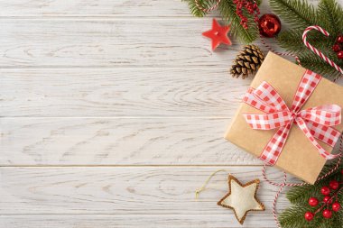Kırsal Noel hediyesi kahverengi kağıda sarılı kırmızı bir kurdele, ahşap bir masanın üzerinde şenlikli bir dekor ile çevrili.