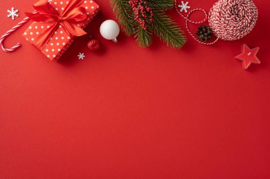Şenlikli bir Noel süslemesi, sarılı bir hediye ve canlı kırmızı bir arka planda süsler. Tatil temaları ve mevsimlik kutlamalar için mükemmel.