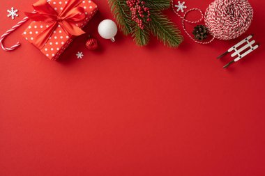 Parlak renkli Noel süslemeleri ve klasik kırmızı arka plan hediyeleri bayram neşesini ve tatil ruhunu çağrıştırıyor.