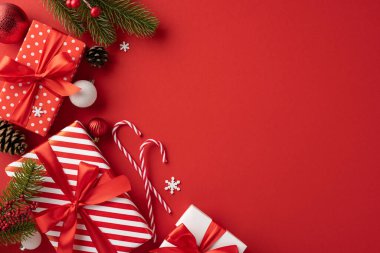 Kırmızı kurdeleli şık Noel hediyeleri ve canlı kırmızı arka planda çeşitli şenlikli dekorasyonlar, sıcaklığı ve bayram neşesini iletiyor.