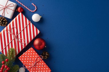 Kırmızı ve beyaz desenli, çam kozalakları ve takılar içeren mavi arkaplandaki Noel hediyelerinin ve dekorasyonların tepeden tırnağa görünümü