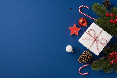 Güzel paketlenmiş bir Noel hediyesinin üst görüntüsü kırmızı kurdeleyle çevrili bayram süsleri ve çam dalları bir tatil havası yaratıyor.