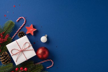 Etrafı çam dalları, baston şekerler ve lacivert arka plandaki süsler de dahil olmak üzere Noel süsleriyle çevrili güzel bir Noel hediyesi.