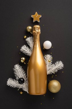 Altın, yıldız ve çam dalları da dahil olmak üzere beyaz bayram süslemeleri olan zarif dikey şampanya şişesi siyah bir arka planda Noel ağacı yapıyor.