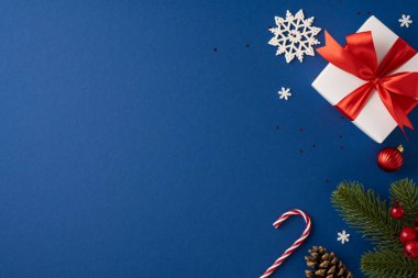 Mavi arka planda kar taneleri, şeker kamışı ve kozalaklarla çevrili kırmızı kurdeleli güzel bir Noel hediyesi.