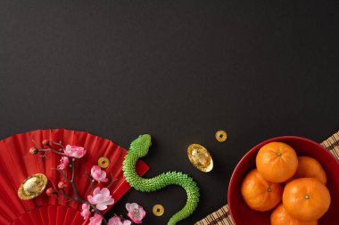 Geleneksel Çin yeni yıl sembolleri, mandalina portakalları, kırmızı yelpaze ve siyah arka planda altın sikkeler, refahı ve kutlamaları simgeliyor.