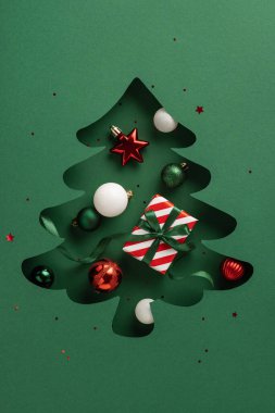 Kırmızı ve yeşil süslemeleri süslemeli bir hediye kutusuyla süsleyen bir Noel ağacının yeşil kağıt dikey kesimi. Bayram kutlamaları için ideal, neşeli ve neşeli duygular iletmek için.