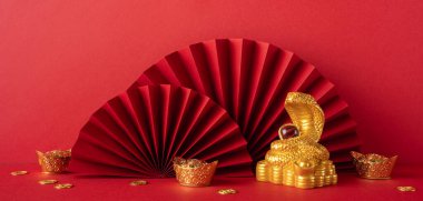 Kırmızı ve altın madalyalar Çin Yeni Yılı sembolize ediyor, altın bir yılan, yelpaze ve parlak bir arkaplan üzerinde paralar