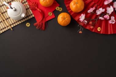 Portakal, kırmızı zarf gibi Çin Yeni Yıl unsurları ve refah ve geleneği simgeleyen siyah bir arkaplanda çaydanlık içeren şenlikli bir üst görünüm düzenlemesi.