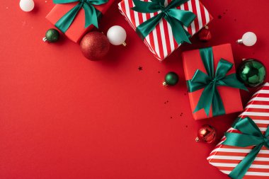 Güzel paketlenmiş Noel hediyeleri yeşil kurdelelerle çevrili, kırmızı arka planda şenlikli süsler, neşeli bir tatil atmosferi yaratıyor.