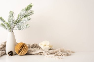 Minimalist yan bakış açısı İskandinav Noel dekoru vazoda buzlu çam dalları, rahat örgü battaniye ve sıcaklık ve kış zarafetini yansıtan geometrik süsler