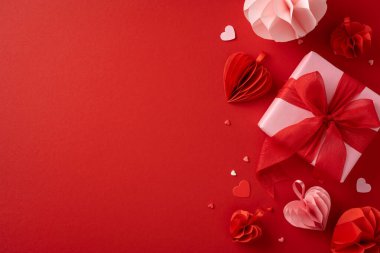 Güzel paketlenmiş bir Sevgililer Günü hediyesi. Kırmızı arka planda kalp şeklinde süslemelerle çevrili kırmızı bir kurdele.