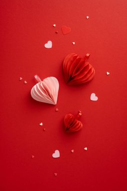 Kırmızı dikey arkaplanda kağıt kalpler ve konfeti romantik ve zarif bir sevgililer günü süsü oluşturur. Kutlamalar ve aşk ifadeleri için mükemmeldir.